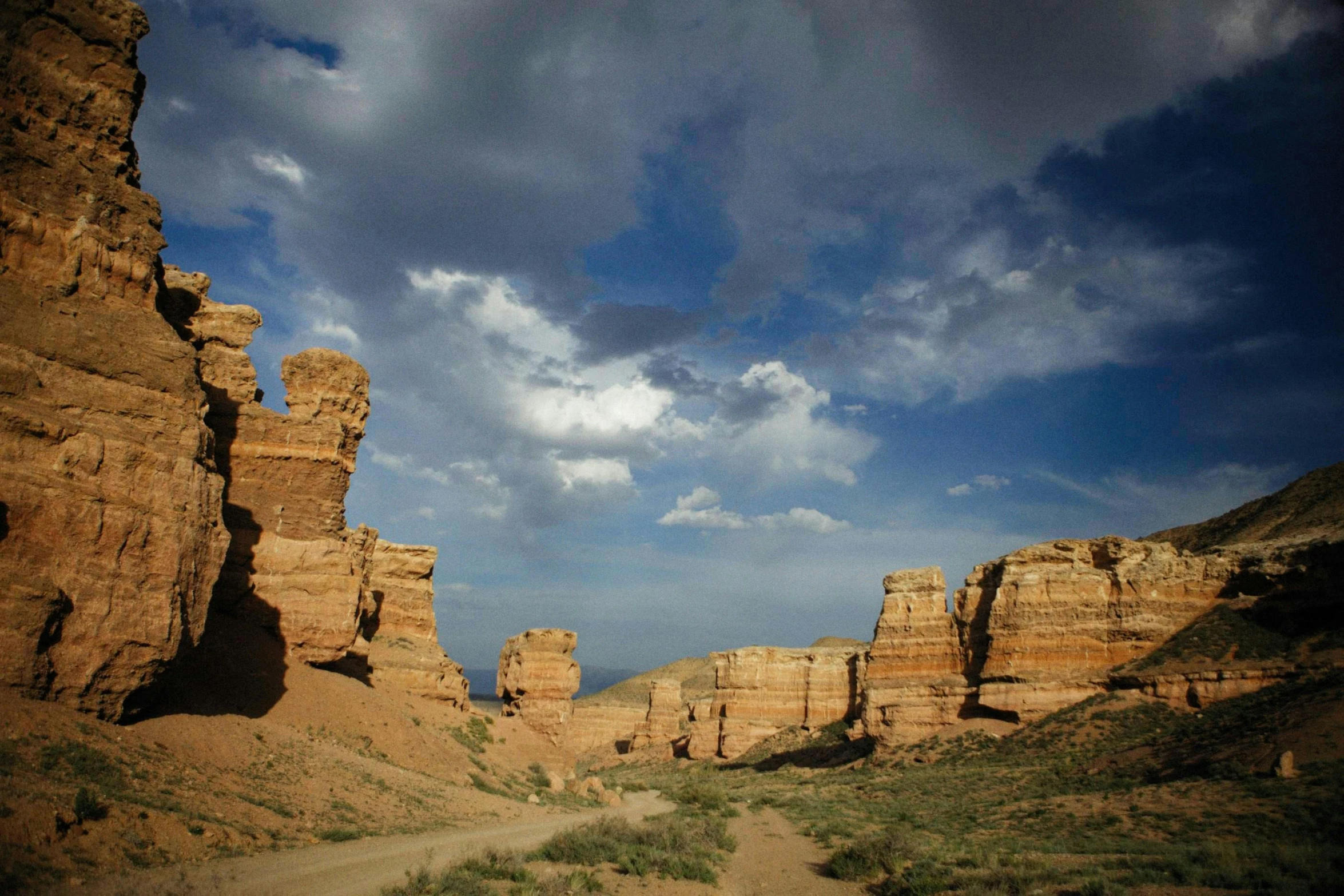 a dirt road through the desert with cliffs in the background