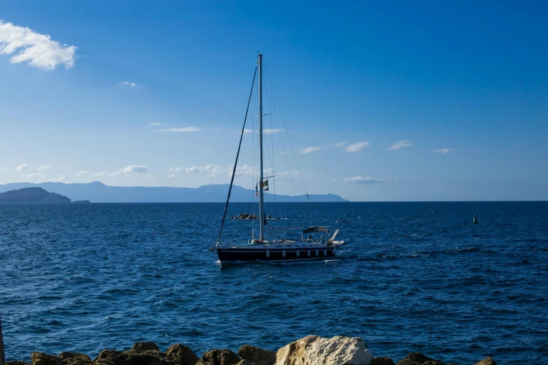 a sailboat traveling through the ocean with some rocks