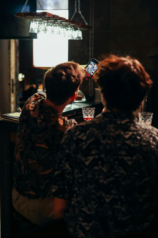 two men sitting at a bar watching television and drinking drinks