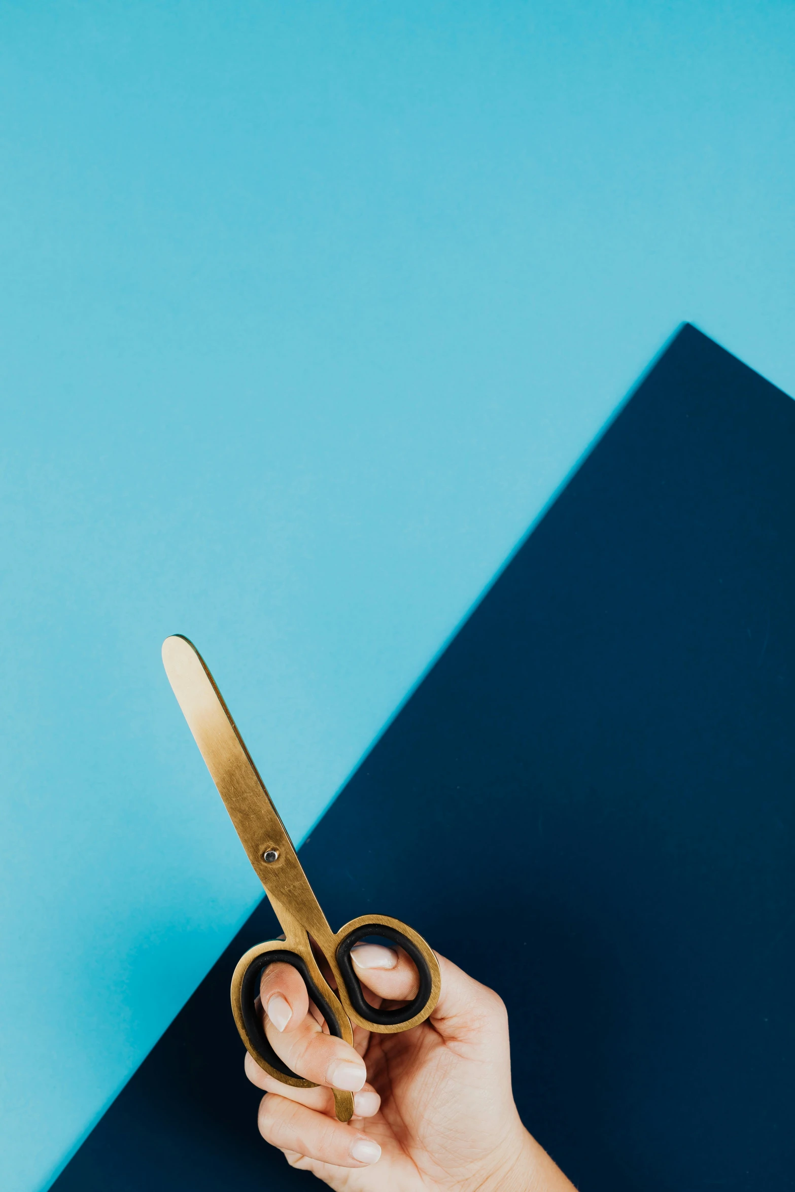 a person holding a gold scissors on a blue background