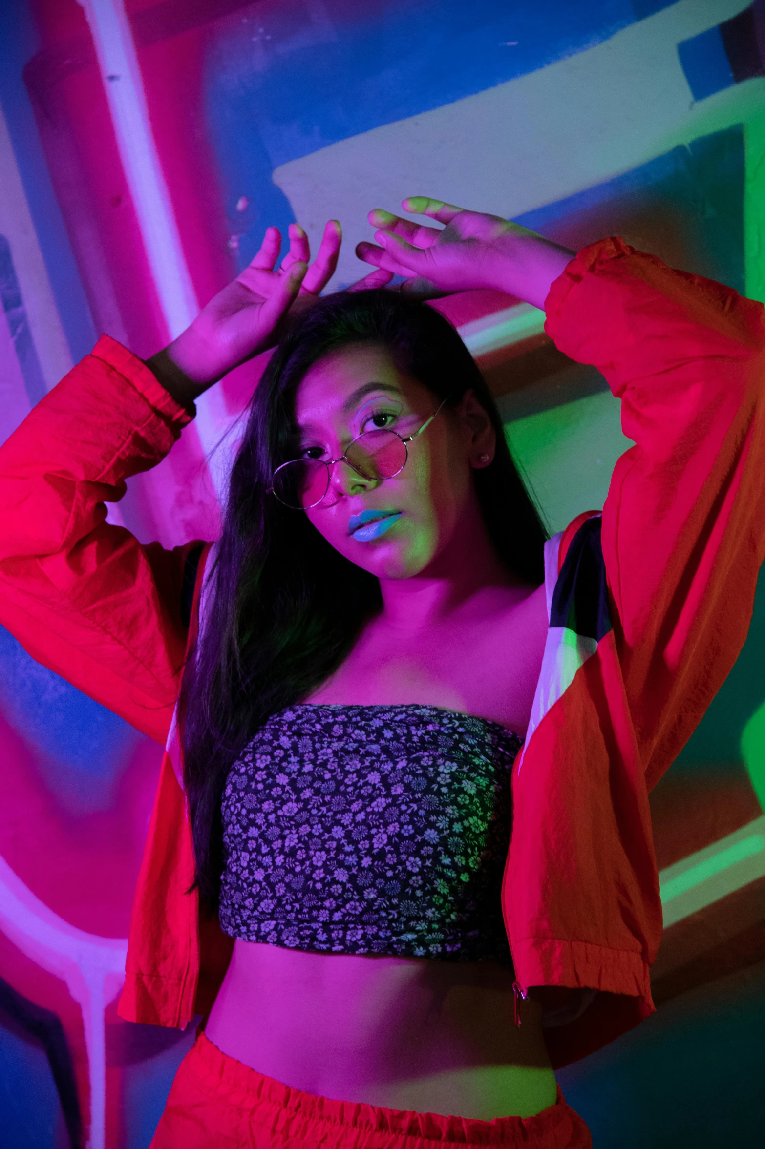 a woman with bright makeup and red clothing in front of a neon colored wall