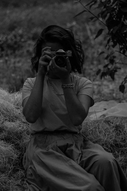 the girl is sitting in the field taking pictures with her camera