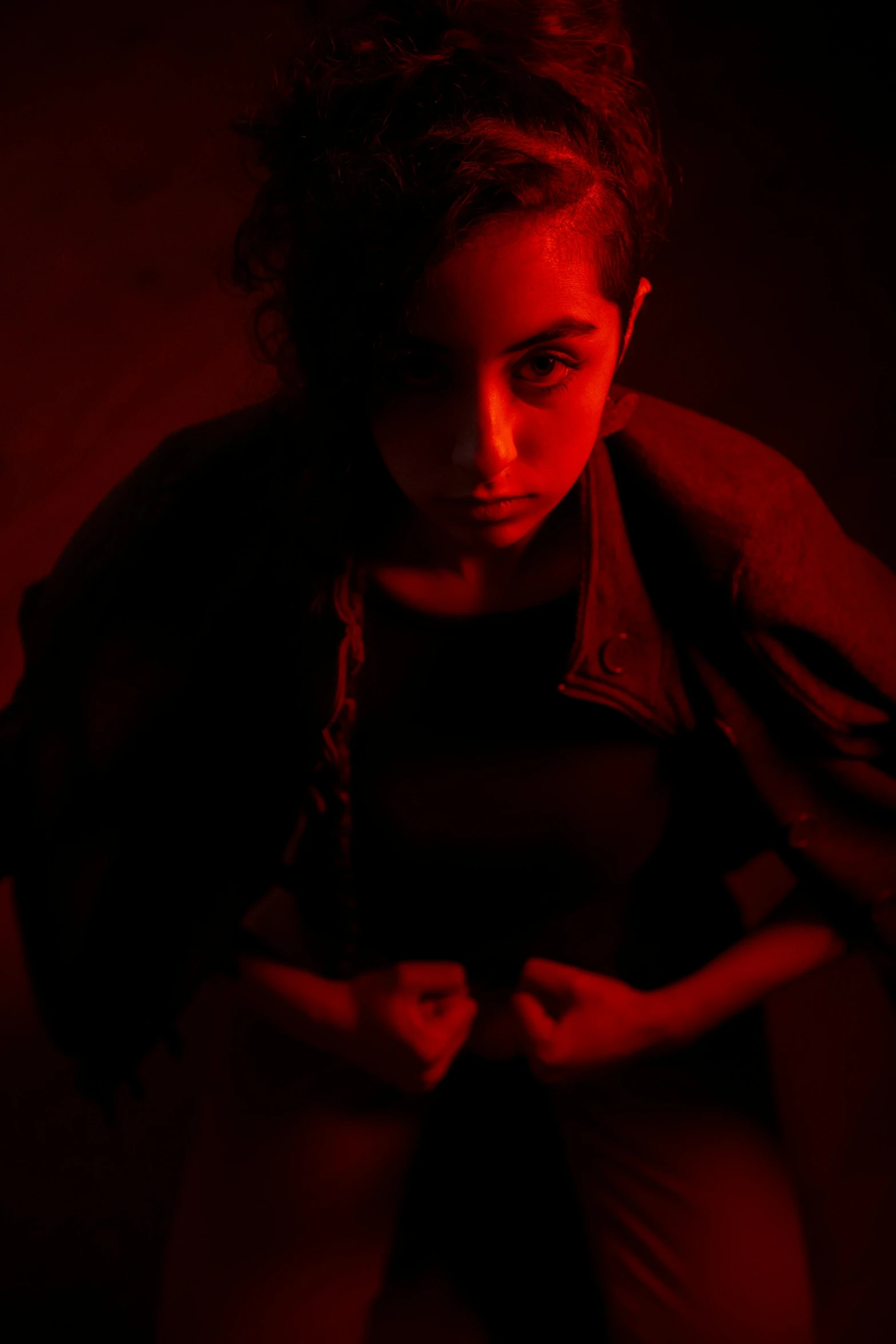 a girl sitting in the dark holding her hands behind her back