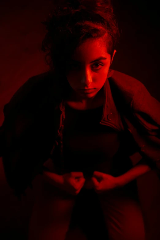 a girl sitting in the dark holding her hands behind her back