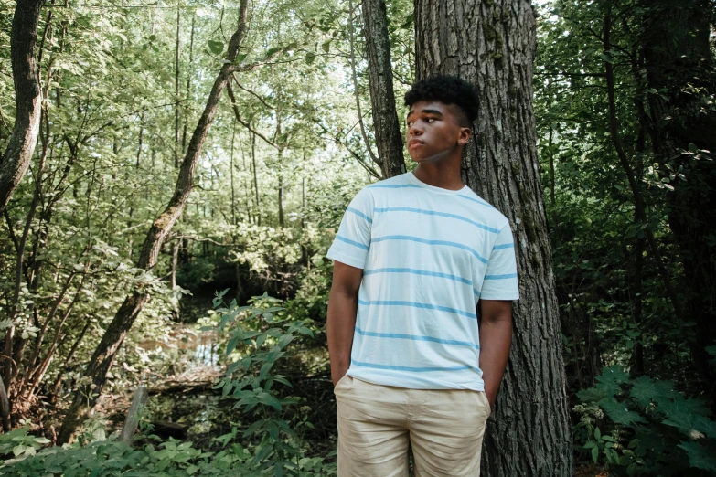 a young man standing in the woods near a tree