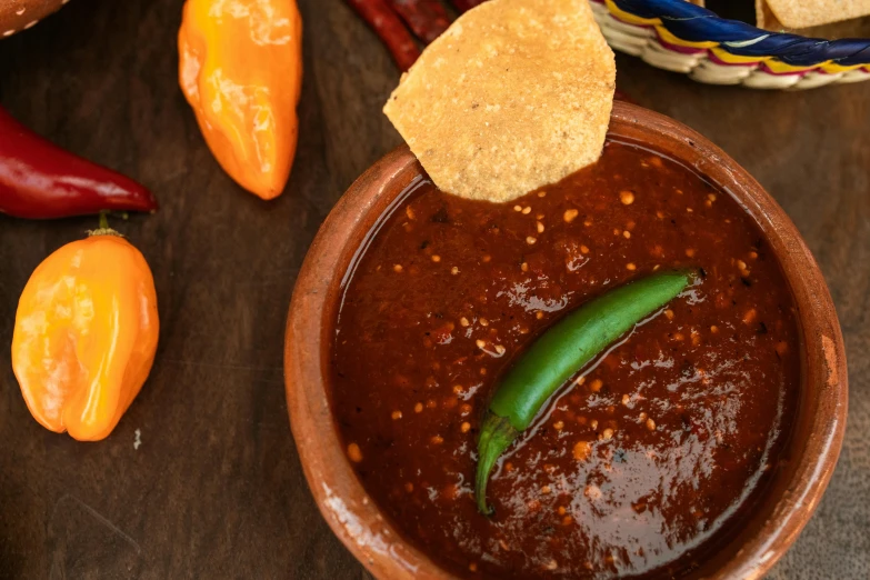 a small brown bowl full of chili sauce next to a stack of mexican bread