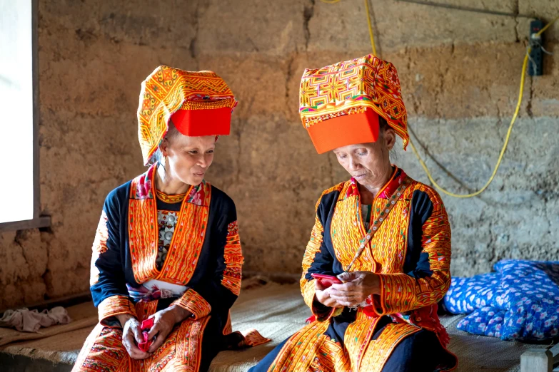 two ladies dressed in colorful attire sitting on a bench