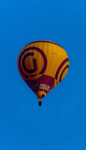 a yellow and brown balloon flying through the blue sky