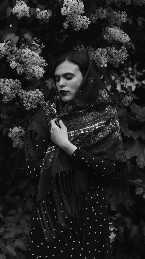 a woman in black dress standing next to a bush