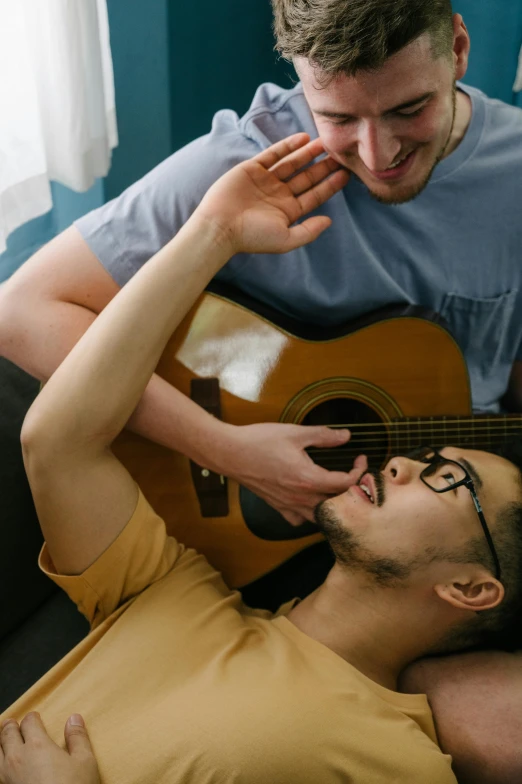 two men sitting on a couch while one man holds an acoustic guitar