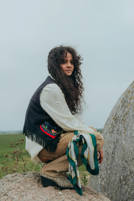 a woman is sitting on a rock with long curly hair