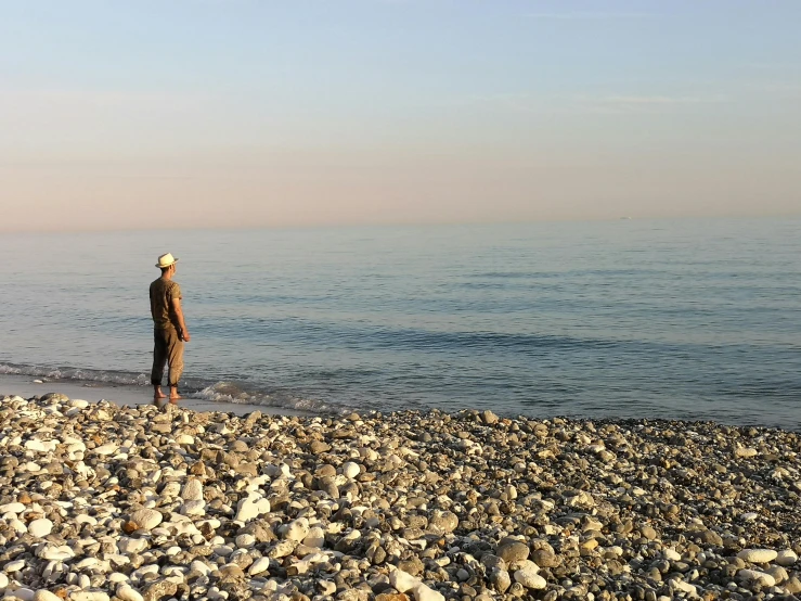 an older man standing on rocky beach, looking out to sea