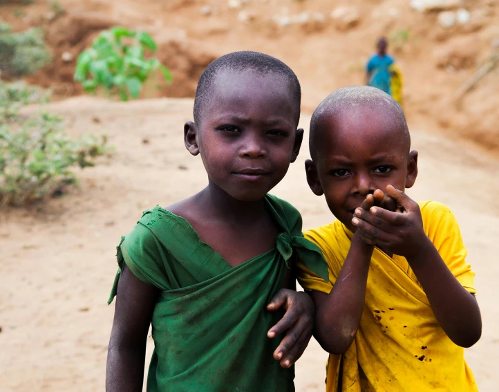 two children standing close to each other with dirt ground in background