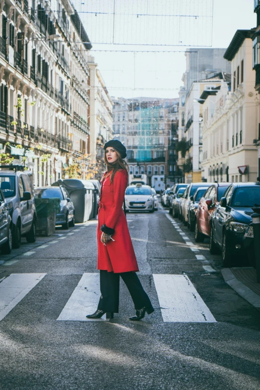 a woman in red coat crossing street in city