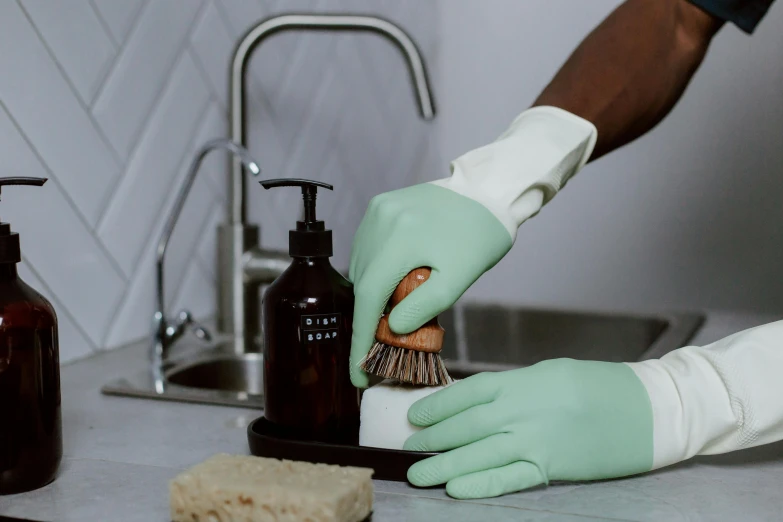 someone holding a scrubbing glove over a bottle next to soap on a kitchen counter