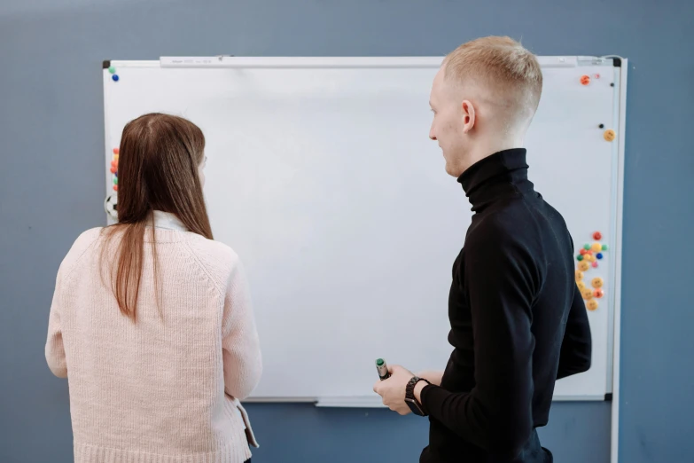 two young people looking at a whiteboard and marker