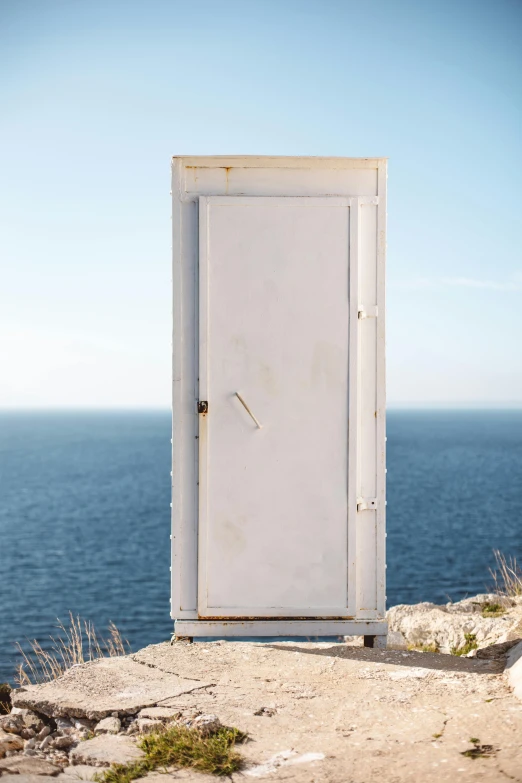 a closed out door stands in a dirt field by the ocean