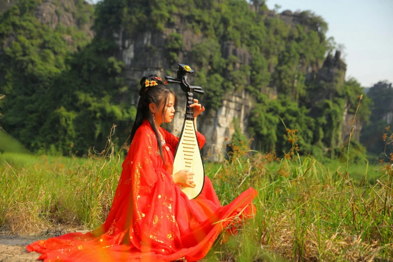 a woman with an oriental hairstyle sitting on the ground in front of mountains