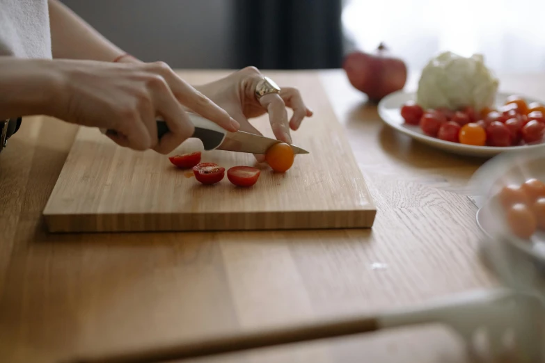 a woman in white shirt holding a knife near sliced tomatoes