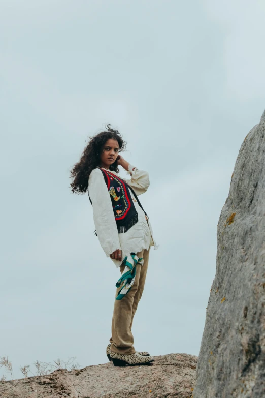 a woman in white jacket standing on rocks talking on cellphone