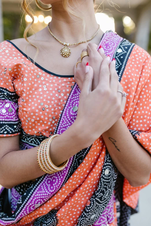 close up of woman wearing multicolored dress with gold rings holding out her hand