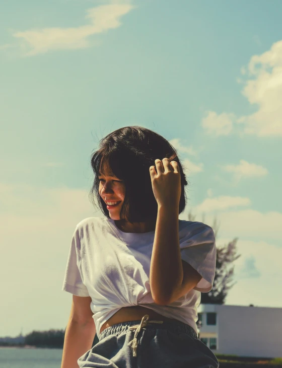 a woman in shorts and a white t - shirt smiles at the camera while talking on a cell phone