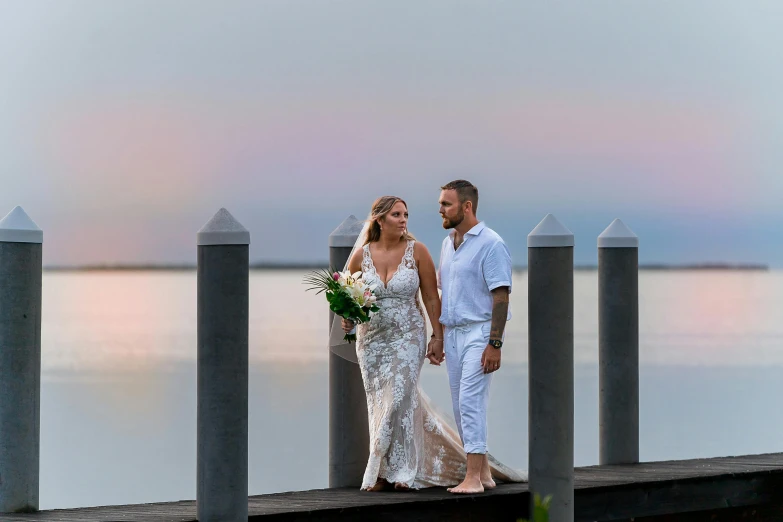 a bride and groom standing on a pier holding hands