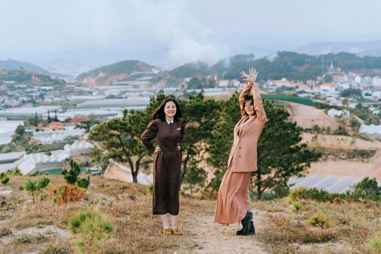 two women on a hill are reaching up toward the sky