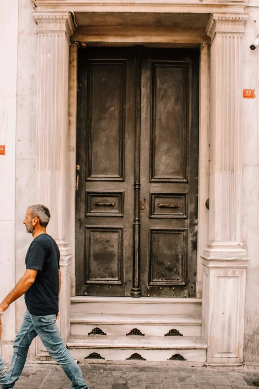 a man walking down a street past a tall wooden door