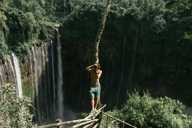 a man stands on top of a log by a waterfall