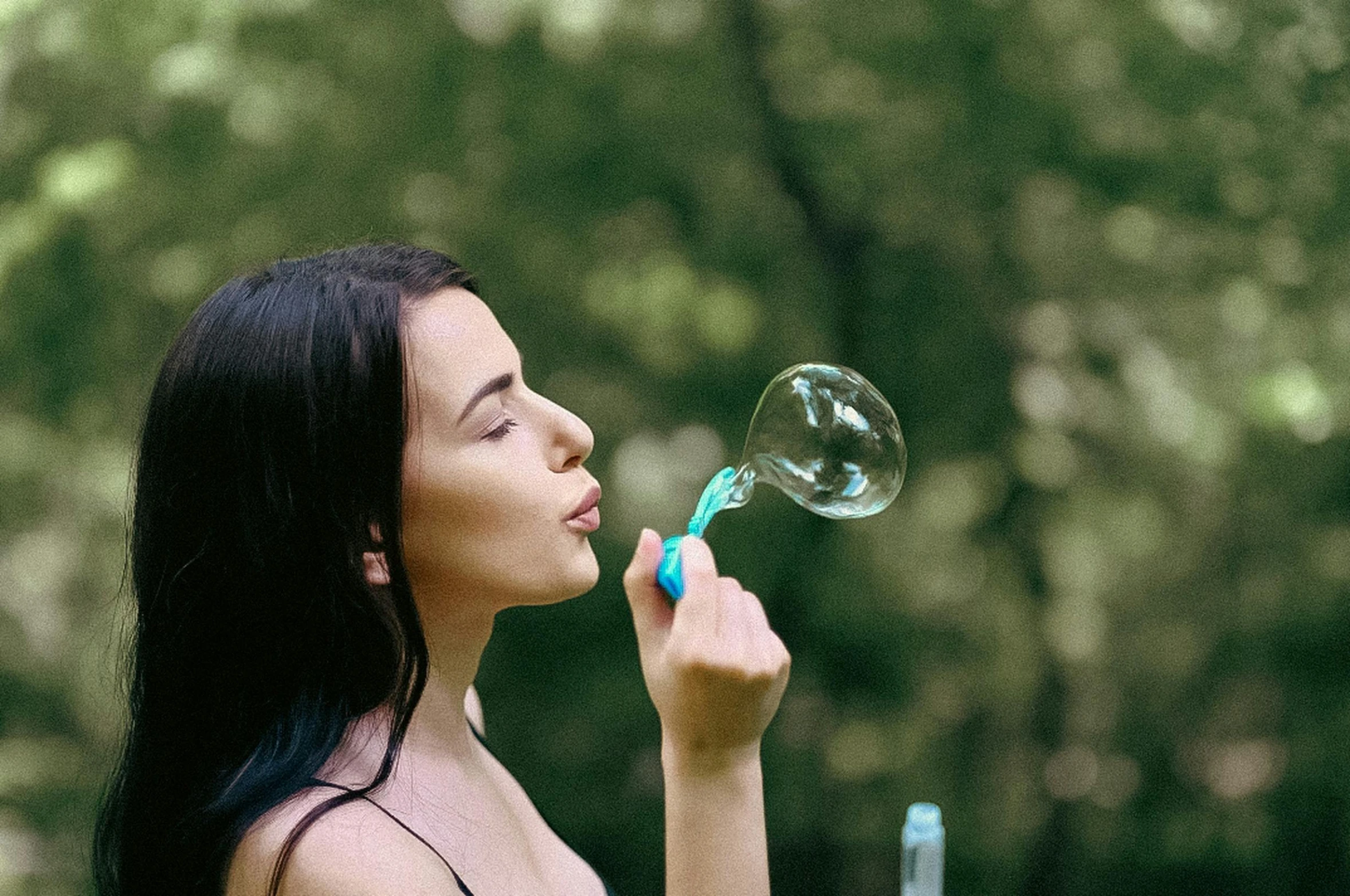 woman with blue and green hair blowing bubbles in front of trees