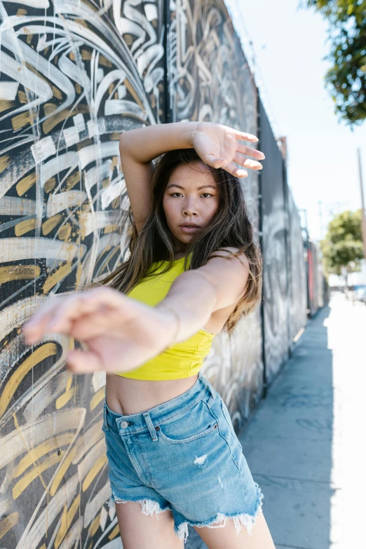 a woman standing near a graffiti covered wall, reaching up to her arm