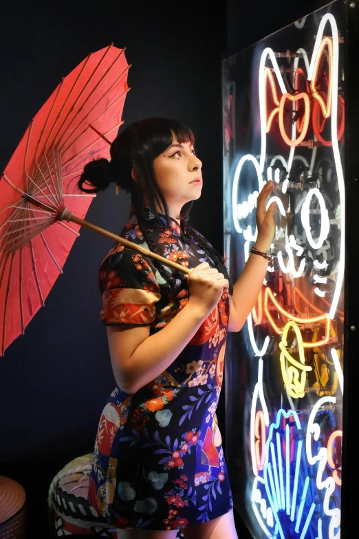 the woman is holding an umbrella near a lit up wall