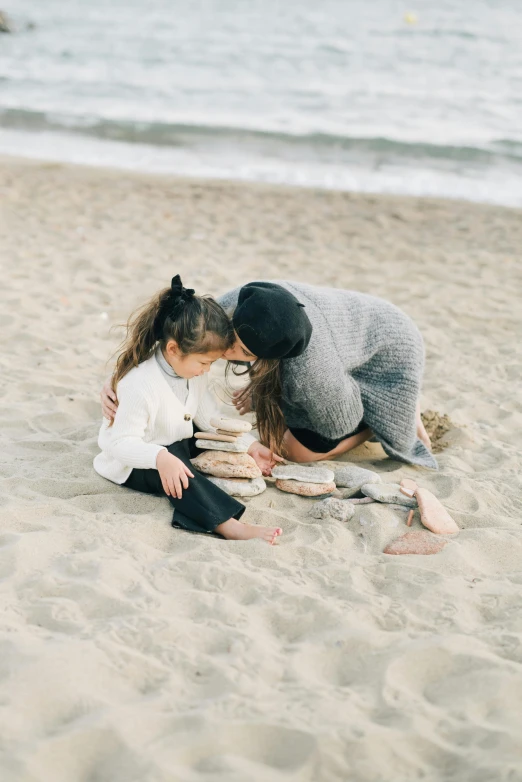 a woman and girl playing in the sand on the beach