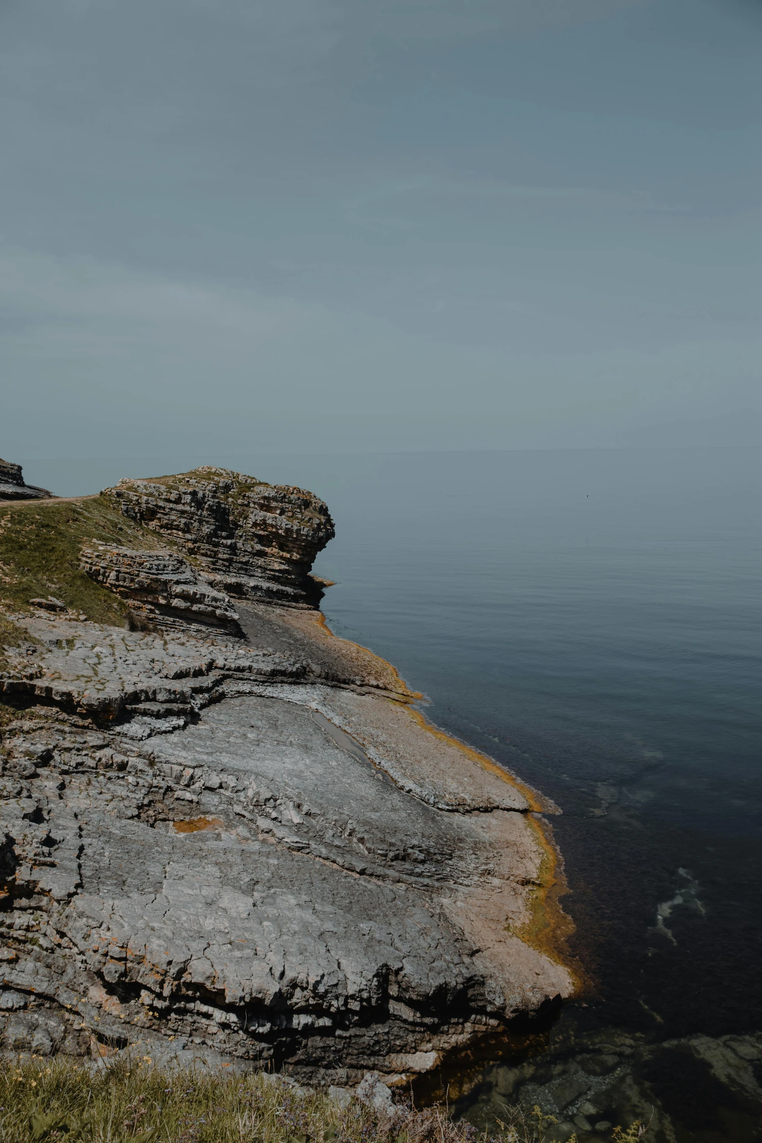 a large rock sitting on top of a rocky cliff next to the ocean