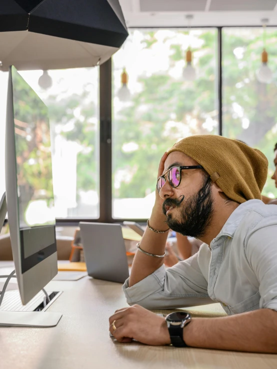 two men wearing glasses are sitting in front of computers