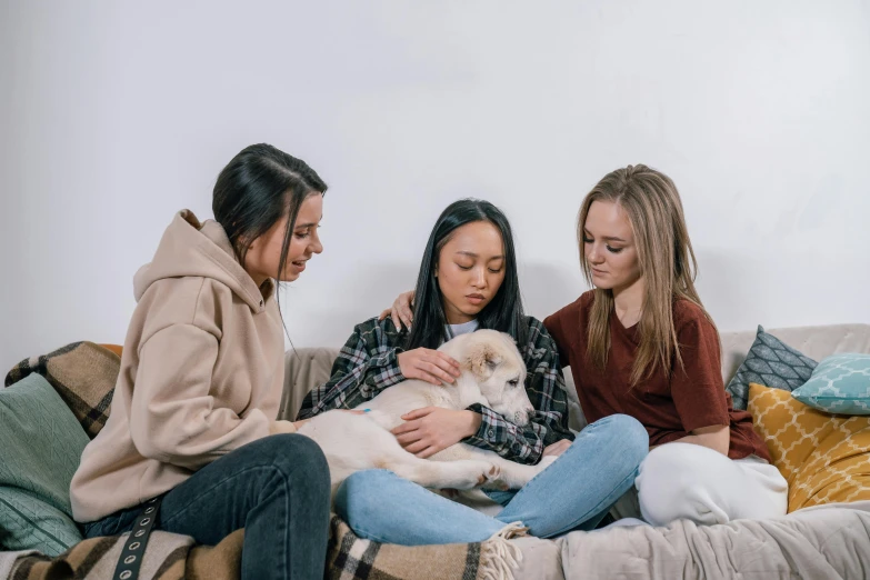 three women sit on a couch together with a dog