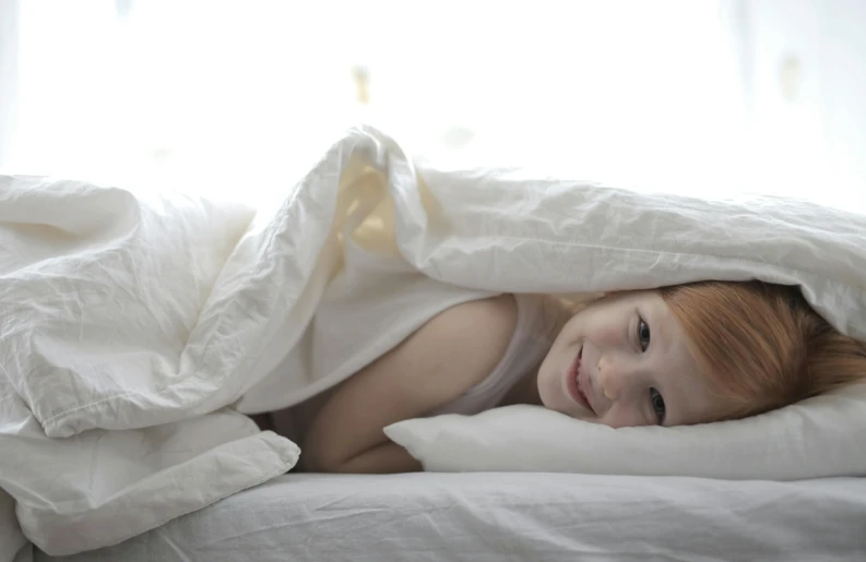 a little girl laying under a blanket on a bed