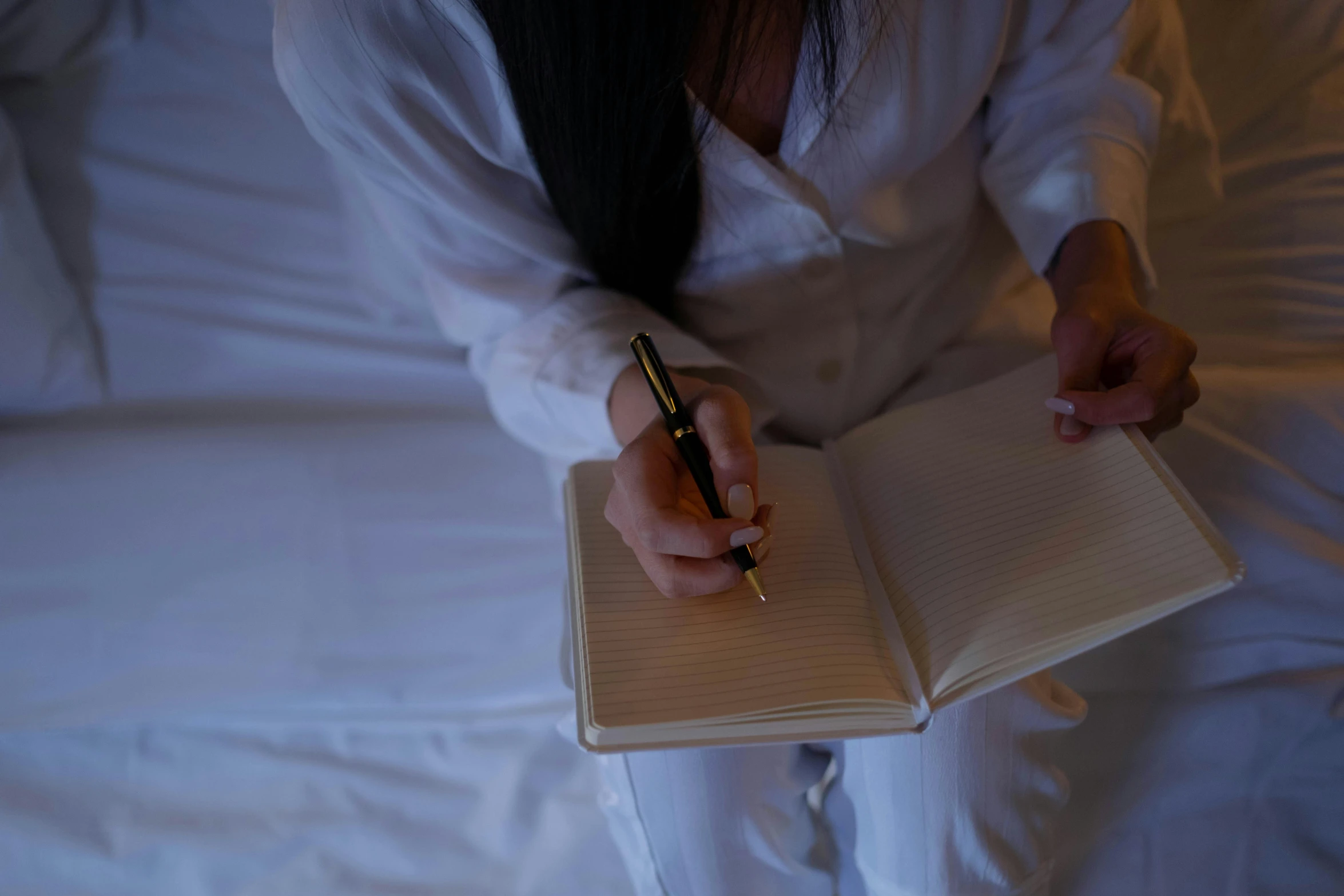 a person writing in a notebook on a white bed