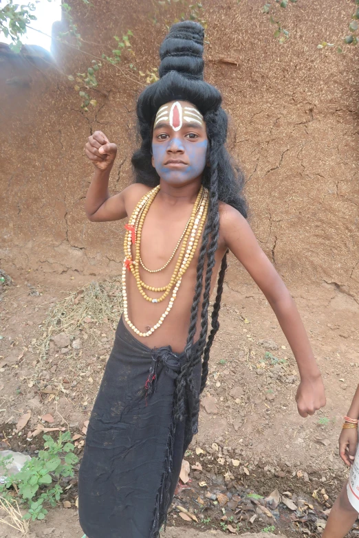 a boy with a black head dress and blue makeup standing in the dirt