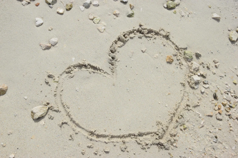 heart drawn in the sand with rocks and pebbles on it