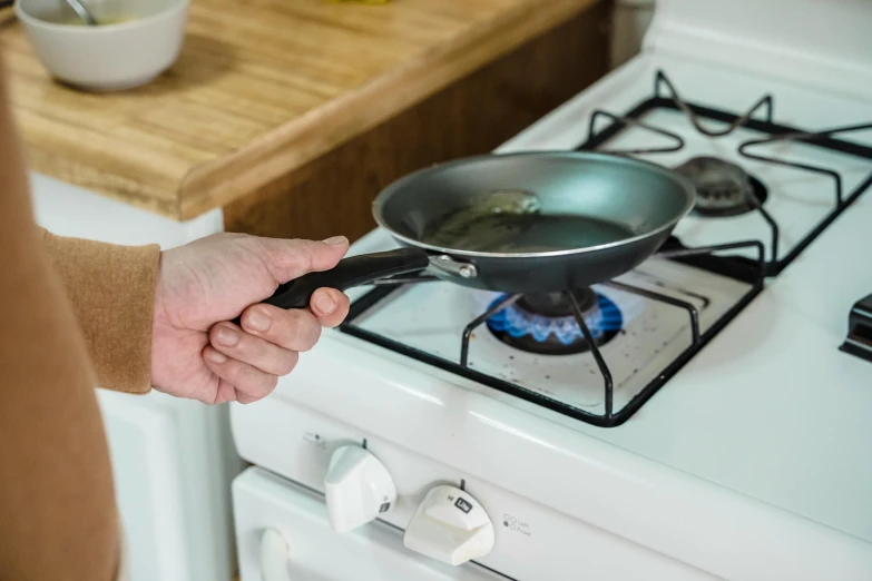 a person holding a frying pan over a stove