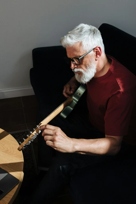 a man with white hair sitting down playing a guitar