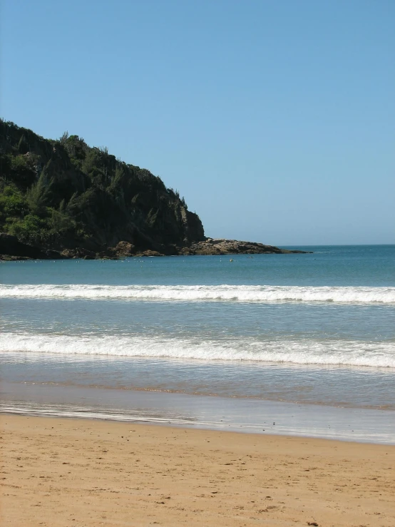 a sandy beach with waves coming in and an island in the distance