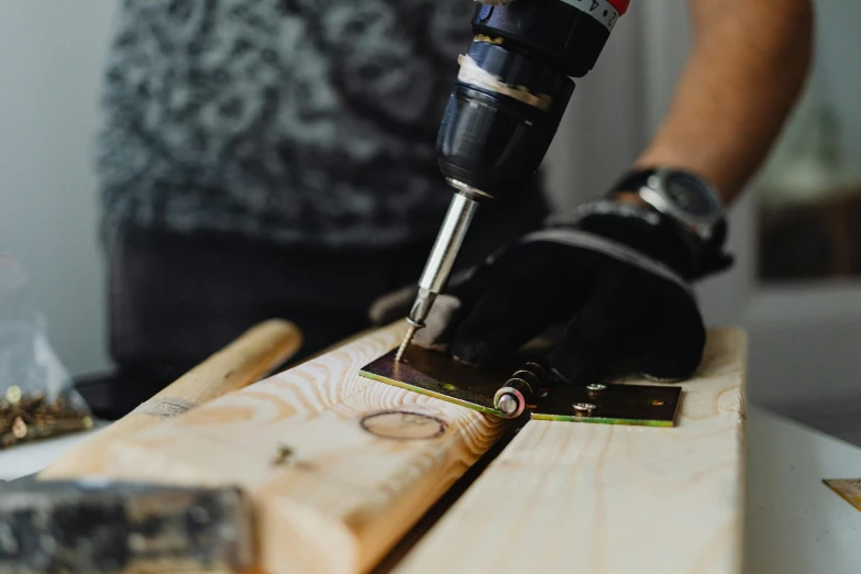 a person uses a drill on wood being held