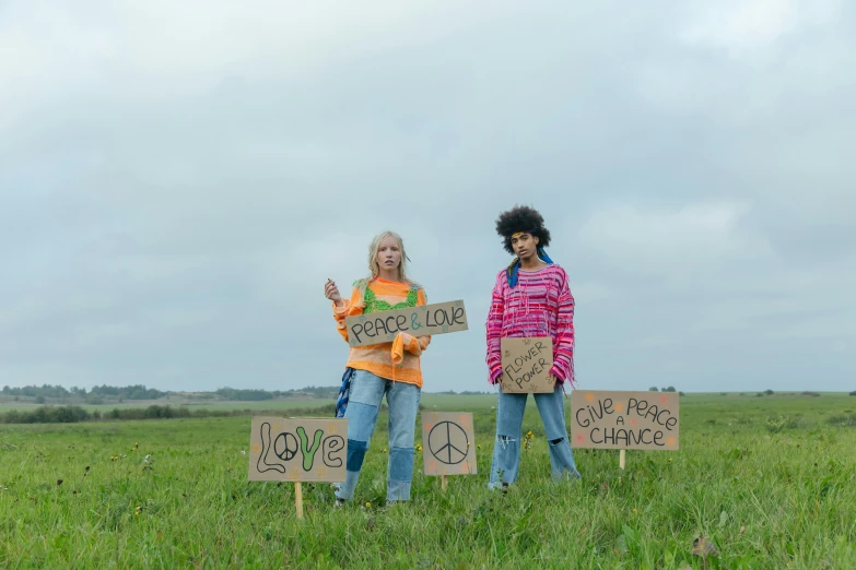 two people holding signs in a field while pointing at them