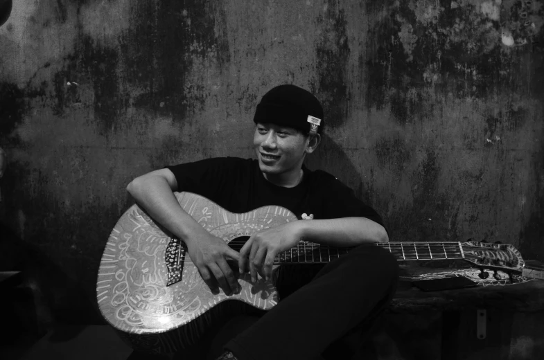 man playing an acoustic guitar by a wall