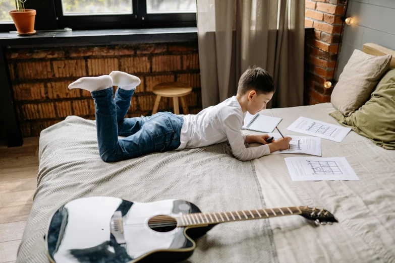 a young man laying on his bed reading while holding an envelope and looking at his music work