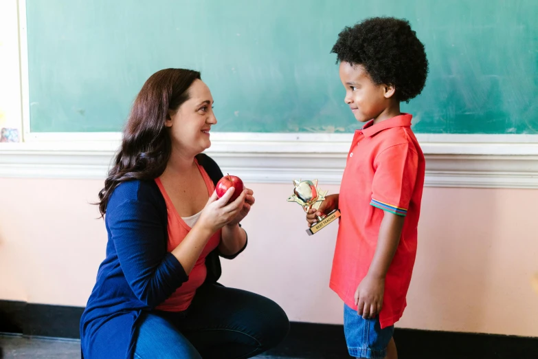 a lady with an apple standing in front of a little boy