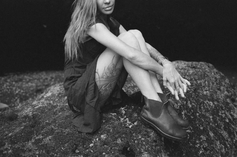 a woman sits on a rock with one hand outstretched